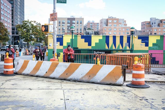 a white and orange construction berm in front of a Lexington Ave subway station